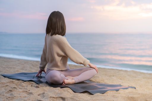 A Hispanic female in a sporty outfit doing some yoga at a beach