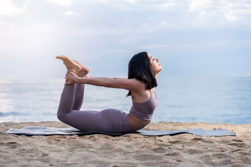 A Hispanic female in a sporty outfit doing some yoga at a beach
