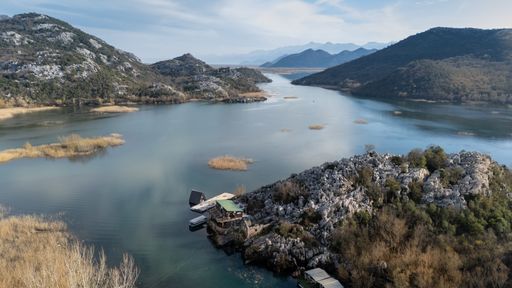 Scenic view of Lake Skadar with surrounding mountains and a small dock in Montenegro, under a clear blue sky.
