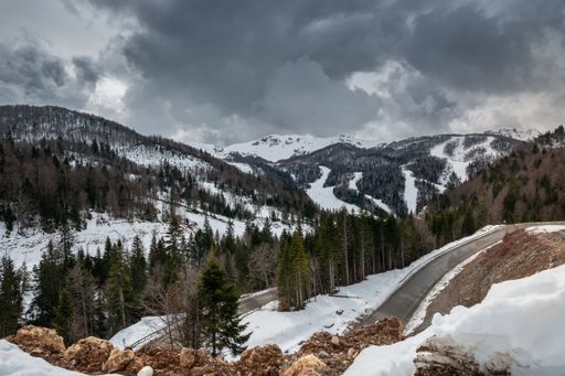 Snow-covered mountains with a winding road under a cloudy sky, showcasing a serene winter landscape.