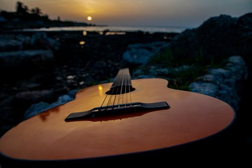 A closeup shot of a brown wooden guitar lying on the rocks at the seaside during late sunset in Havana, Cuba