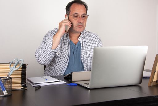 A Spanish businessman talking on the phone with a client while working on his laptop in the office