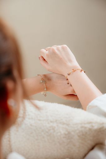 Close-up of two hands wearing delicate charm bracelets with a soft focus background, showcasing elegant jewelry design.