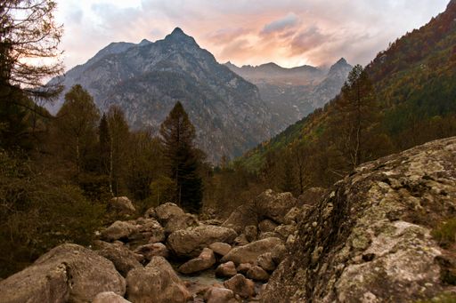 A landscape of rocky mountains covered in forests under a cloudy sky during the sunset in the evening
