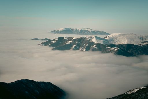 A reathtaking view of snow-capped mountains emerging through a sea of clouds under a clear blue sky.