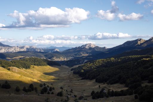A high angle shot of mountainous landscape with peaks and a plato in the foreground under sunlight