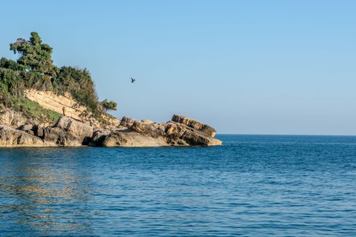A serene coastal landscape with rocky cliffs and a bird in flight over calm blue waters under a clear sky.