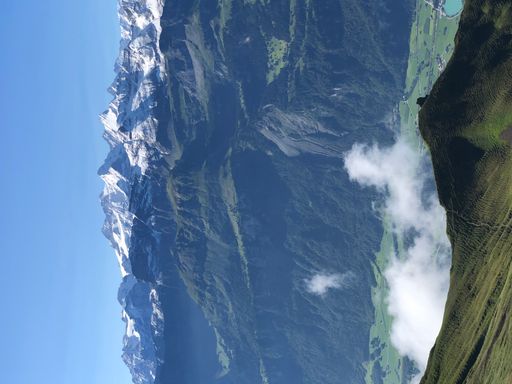 A vertical shot of rocky hills covered in greenery and fog under the sunlight and a blue sky