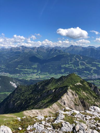A vertical shot of rocky hills covered in greenery under the sunlight and a blue sky