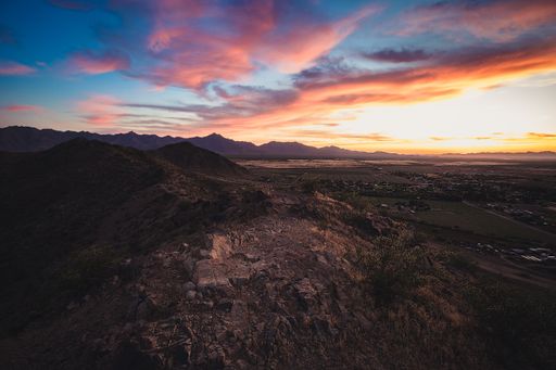 Stunning sunset over a rocky mountain landscape with vibrant clouds and a distant view of a valley below in Phoenix, AZ