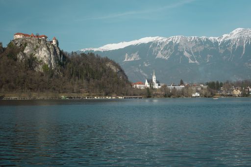 Scenic view of Bled Castle on a cliff overlooking Lake Bled with snow-capped mountains in the background under a clear blue sky