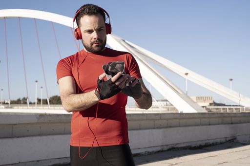 A closeup shot of a male in red headphones using his mobile while jogging in the street