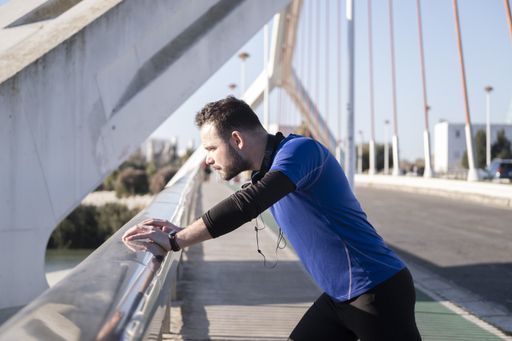 A closeup shot of a young male leaning on the border of the bridge while jogging
