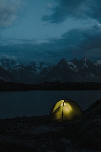 A vertical shot of a tent with lighting on the bay of a lake on the mountains at night