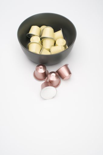 A vertical shot of espresso capsules in a bowl on a white background