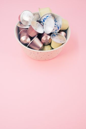 A vertical shot of white espresso capsules in a bowl on a pink background