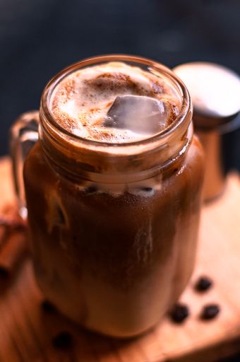 A closeup shot of iced creamy latte coffee mug and roasted beans on a wooden board
