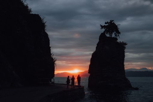 A silhouette of people standing near the Siwash Rock during a beautiful sunset in Vancouver, Canada