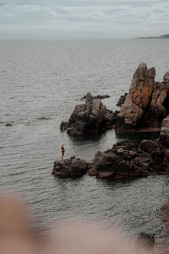 A vertical shot of a male standing on the rock in the gray sea under a cloudy sky