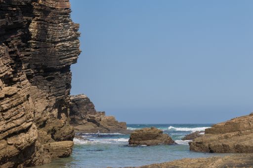 A gorgeous view of a calm sea under a clear blue sky with cliffs sticking out of the water at As Catedrais
