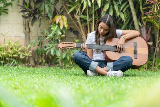 A young girl sitting on the grass and playing guitar