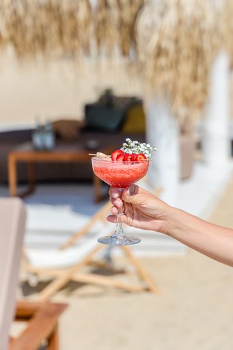 A vertical shot of a woman's hand holding a glass of delicious strawberry cocktail at a sunny beach