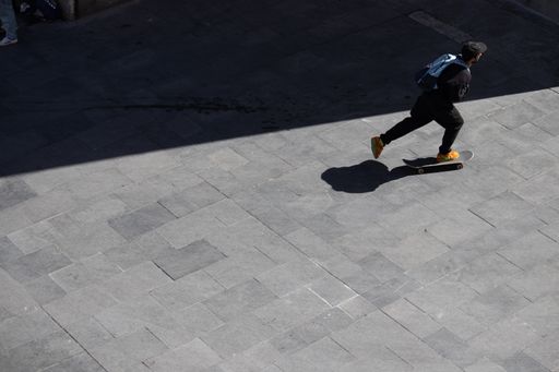 A young male with a backpack riding a skateboard in the street of Barcelona in Spain