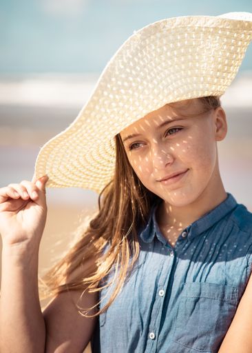 A vertical shot of a Caucasian, attractive young lady with a summer hat on the beach in Netherlands