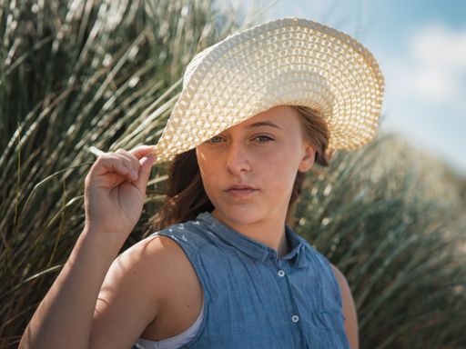 A closeup shot of a Caucasian, attractive young lady with a summer hat on the beach in Netherlands