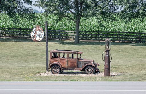 A vintage car and old gas pump in a rural setting with a cornfield background, evoking nostalgia.