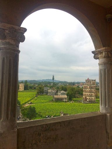 View through an ancient archway showcasing lush green fields and historic buildings in Kaiping, China.