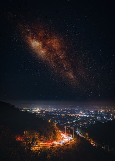 A beautiful view of starry sky and Milky Way over a highway among forested hills against the cityscape