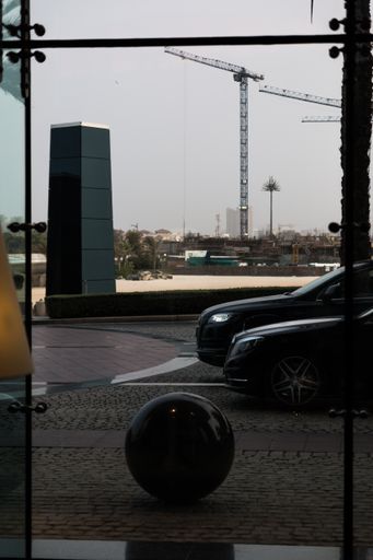 A view from a building's open glass door to a paved road and cars against a construction site