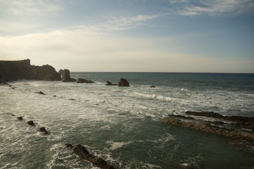 Scenic view of a rocky coastline with waves crashing under a partly cloudy sky, capturing the essence of a serene seascape