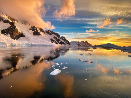 A beautiful view of snow-covered mountains and a frozen lake under a cloudy sky at sunrise