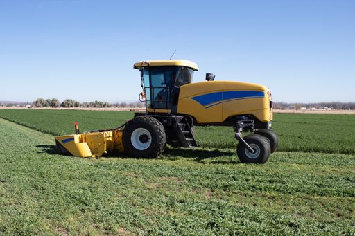 A yellow self-propelled mower in a green agricultural field under a blue clear sky