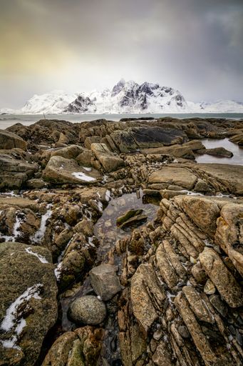 A beautiful vertical image of a rocky Atlantic shore with snow covered mountain in the background