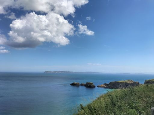 Scenic coastal view with blue sky, clouds, and lush green cliffs overlooking the ocean in Northern Ireland.