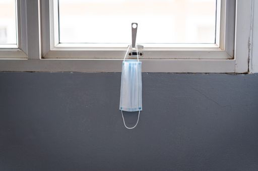A used protective facemask hanging on the window in the building