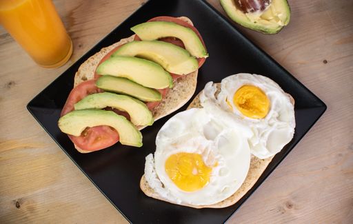 A top view of toasts with omelets, tomatoes, and avocados on a wooden table with a glass of juice