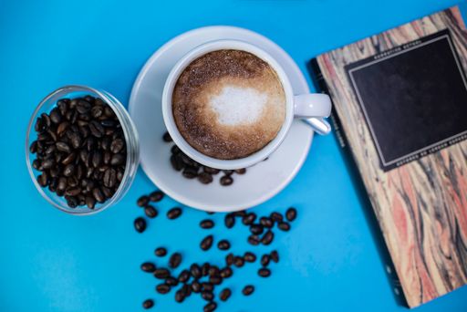 A top view of a cup of coffee, coffee beans, and a book on a blue background