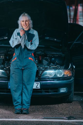 An attractive young blonde female wearing an auto mechanic uniform and repairing the car