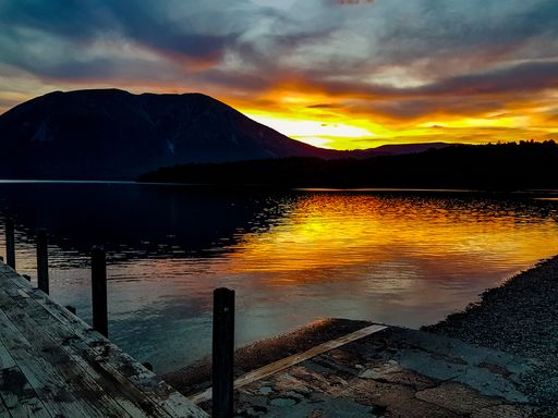 A breathtaking sunset over a tranquil lake with vibrant orange and yellow hues reflecting on the water in New Zealand