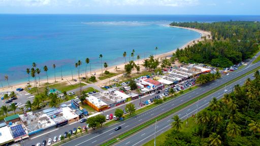 An aerial view of a beautiful blue clean sea with a sandy beach and palm trees in a resort city