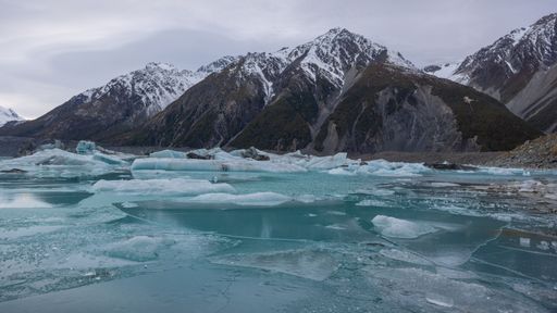 Tasman Lake with frozen icesheets and icebergs overlooked by snow-capped mountains.
