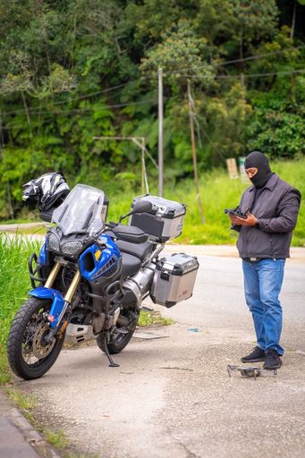 A Yamaha Super Tenere 1200 adventure motorcycle parked at the roadside while a rider prepares to fly a drone.