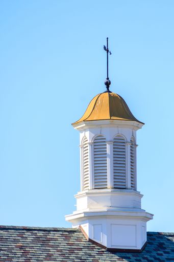A close-up of a white cupola with a golden dome and weather vane against a clear blue sky.
