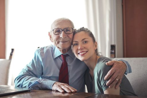 A selective focus shot of an elderly caucasian male hugging a young caucasian female both smiling at the camera
