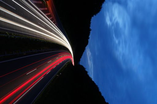 A long exposure of traffic light trails between forested hills during the blue hour