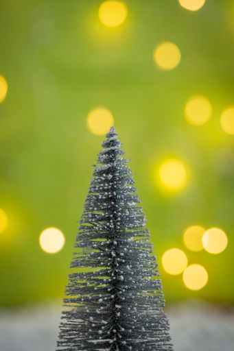 A vertical of a small decorative artificial Christmas tree against the blurry bokeh lights background